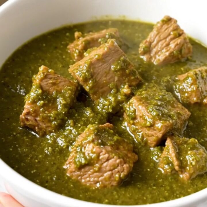 A white bowl filled with steaming, tender pork chunks in a glossy green chile verde sauce.