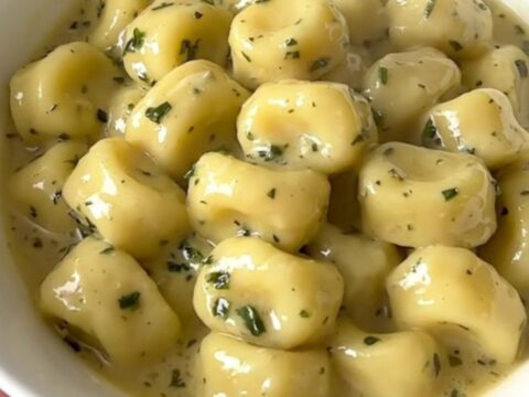 A top-down view of creamy garlic herb gnocchi with mushrooms in a white bowl, steaming and ready to eat.