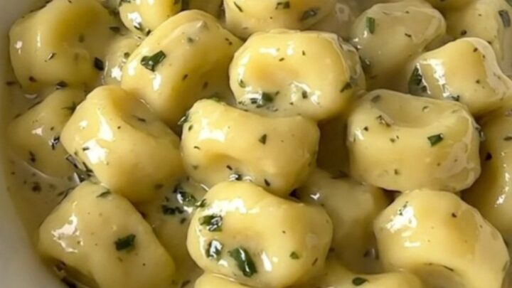 A top-down view of creamy garlic herb gnocchi with mushrooms in a white bowl, steaming and ready to eat.