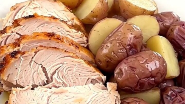 A slow cooker filled with a cooked turkey breast, baby red potatoes, and savory herb broth on a white quartz countertop.