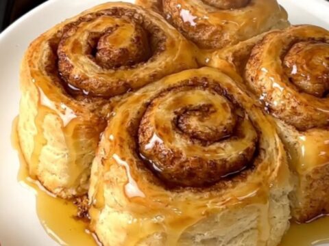 A warm, steaming pumpkin cinnamon roll cobbler served in a white bowl with a spoon.