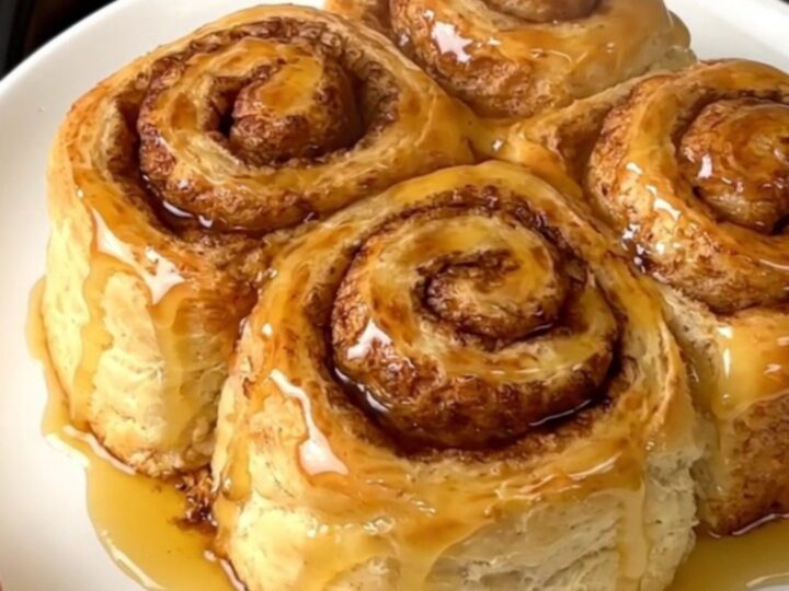 A warm, steaming pumpkin cinnamon roll cobbler served in a white bowl with a spoon.