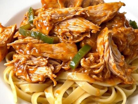 Creamy Cajun chicken alfredo served on a white plate with steaming fettuccine noodles.