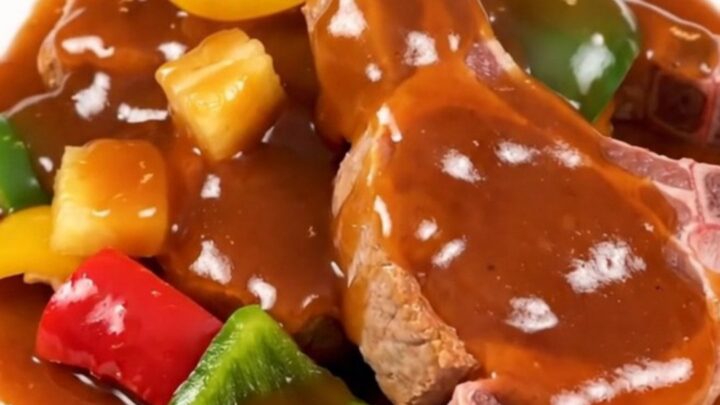 A plate of slow-cooked sweet and sour pork chops with pineapple and bell peppers, steaming hot.
