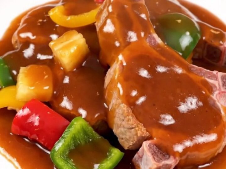 A plate of slow-cooked sweet and sour pork chops with pineapple and bell peppers, steaming hot.
