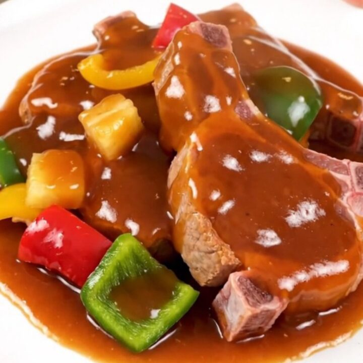 A plate of slow-cooked sweet and sour pork chops with pineapple and bell peppers, steaming hot.