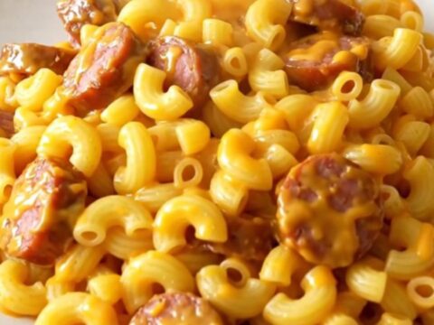 A close overhead view of creamy macaroni and smoked sausage in a black slow cooker.
