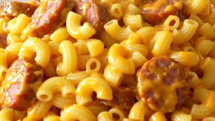 A close overhead view of creamy macaroni and smoked sausage in a black slow cooker.