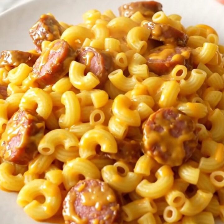 A close overhead view of creamy macaroni and smoked sausage in a black slow cooker.