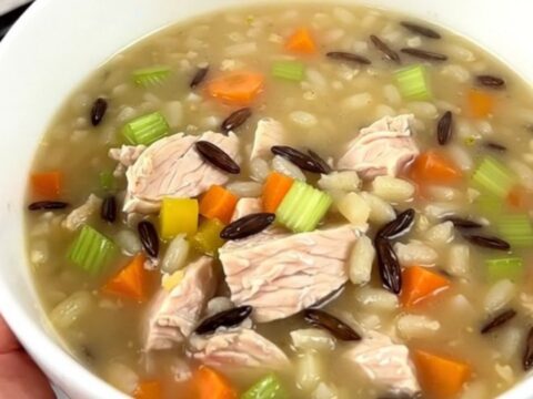 A steaming bowl of creamy chicken and wild rice soup in a white ceramic bowl.