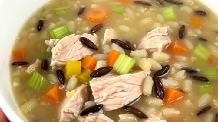 A steaming bowl of creamy chicken and wild rice soup in a white ceramic bowl.