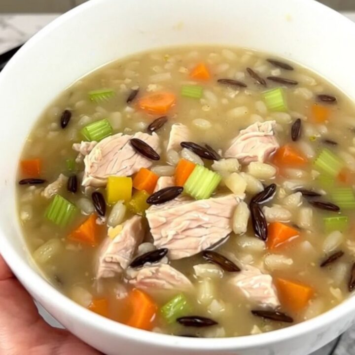 A steaming bowl of creamy chicken and wild rice soup in a white ceramic bowl.