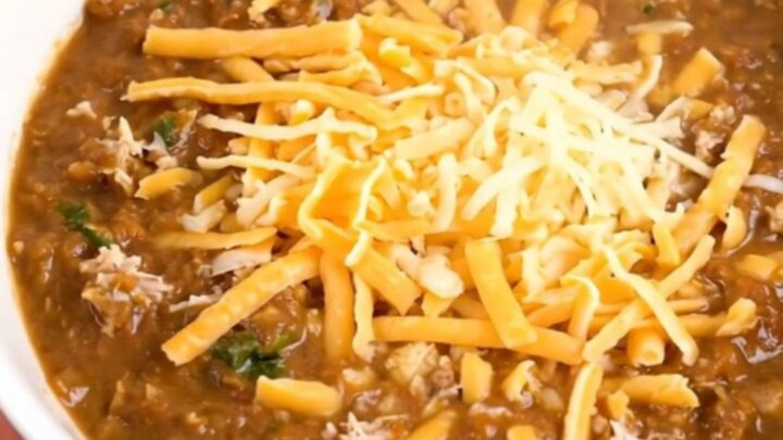A steaming bowl of creamy white turkey chili in a black slow cooker, showing a rich and thick texture.