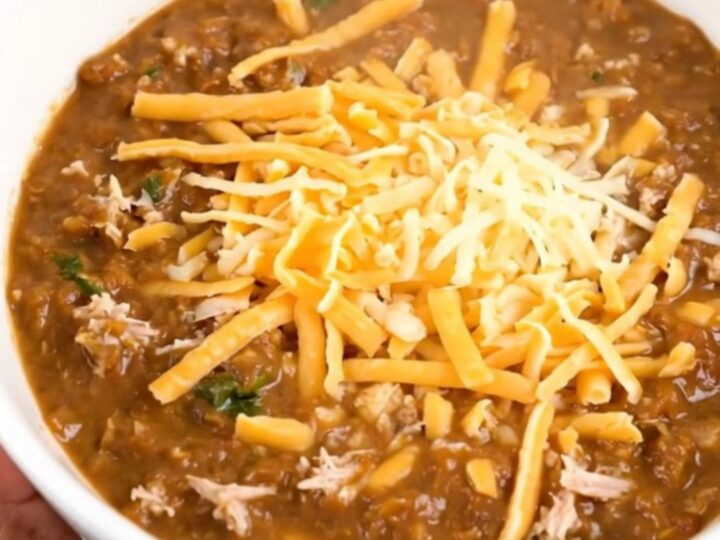 A steaming bowl of creamy white turkey chili in a black slow cooker, showing a rich and thick texture.