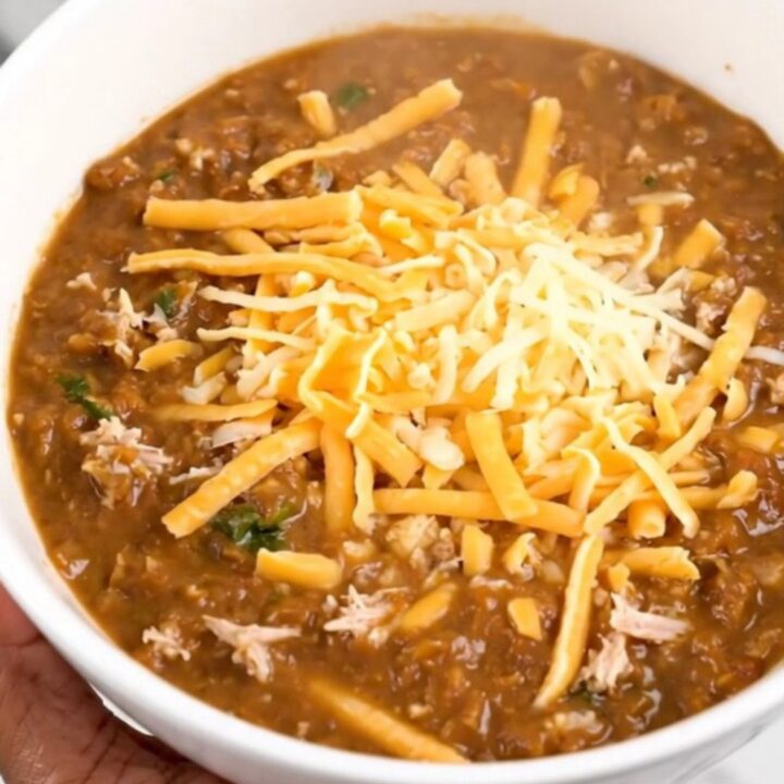A steaming bowl of creamy white turkey chili in a black slow cooker, showing a rich and thick texture.