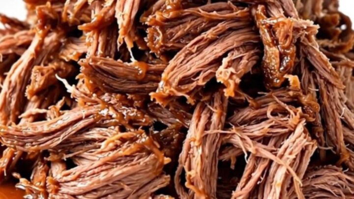 A close-up of a tender, shredded beef chuck roast coated in a rich, dark barbecue sauce on a white plate.