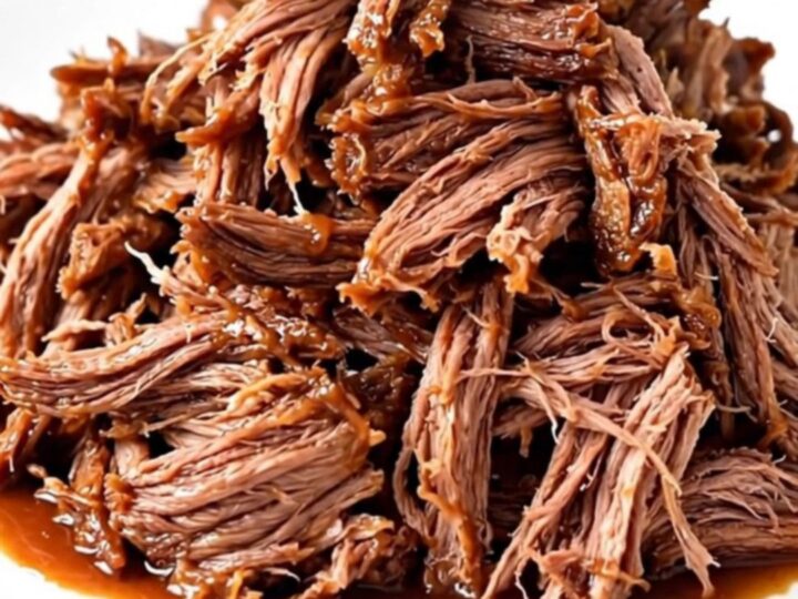 A close-up of a tender, shredded beef chuck roast coated in a rich, dark barbecue sauce on a white plate.