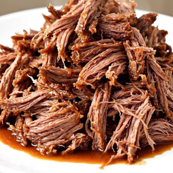 A close-up of a tender, shredded beef chuck roast coated in a rich, dark barbecue sauce on a white plate.