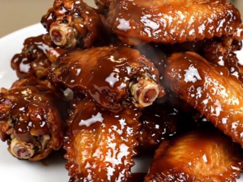 A close-up of glossy, dark-glazed chicken wings in a slow cooker on a white speckled countertop.