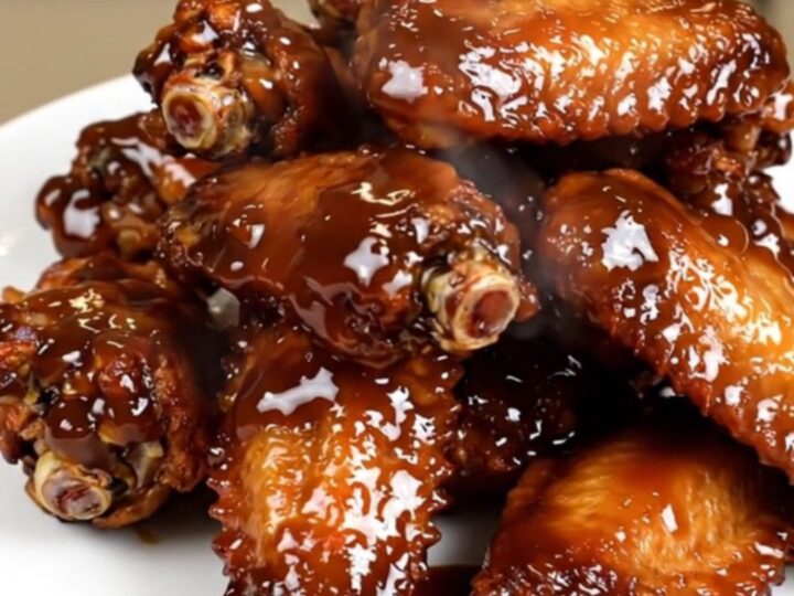A close-up of glossy, dark-glazed chicken wings in a slow cooker on a white speckled countertop.