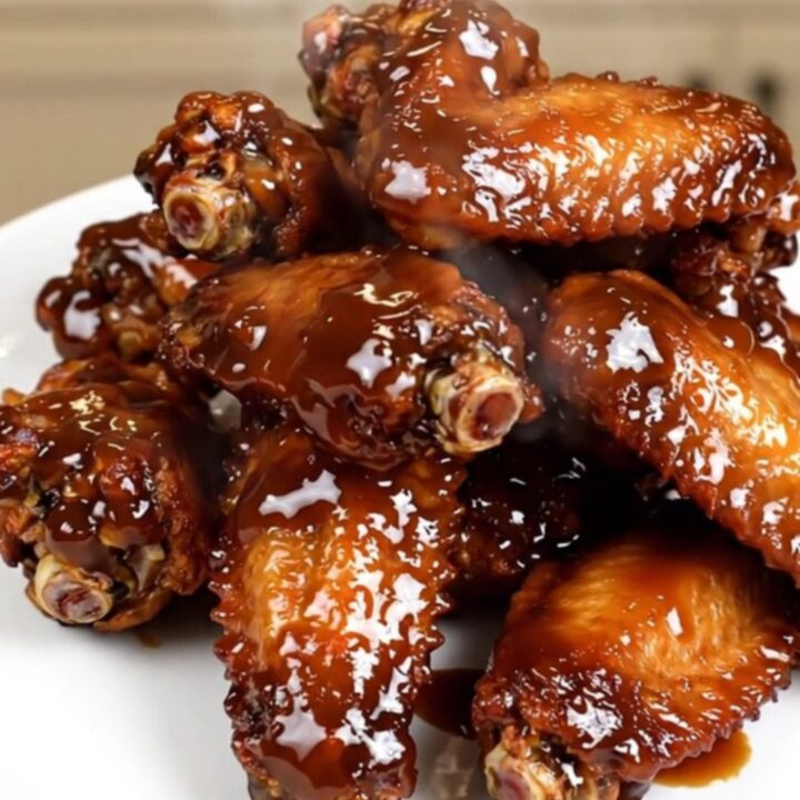 A close-up of glossy, dark-glazed chicken wings in a slow cooker on a white speckled countertop.