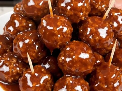 A close-up view of glazed beef meatballs in a slow cooker, glistening with a dark honey and barbecue sauce.