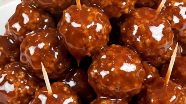 A close-up view of glazed beef meatballs in a slow cooker, glistening with a dark honey and barbecue sauce.