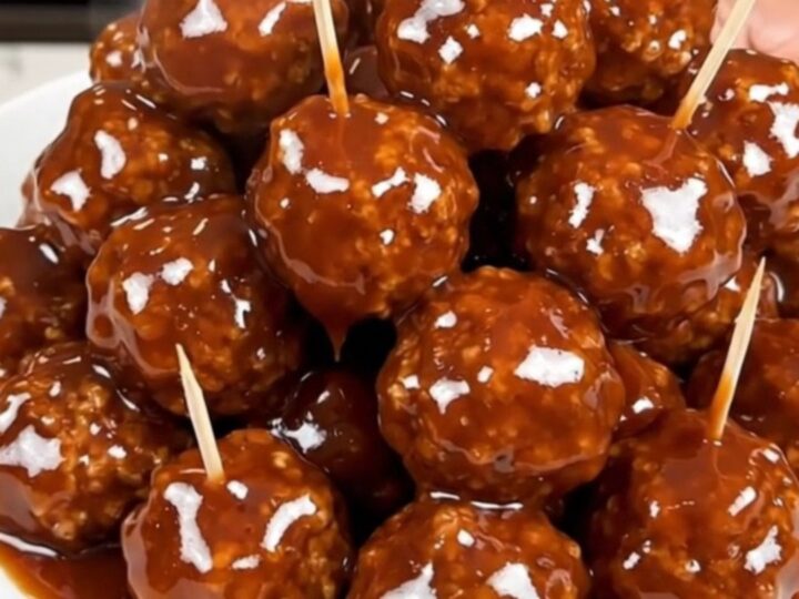 A close-up view of glazed beef meatballs in a slow cooker, glistening with a dark honey and barbecue sauce.