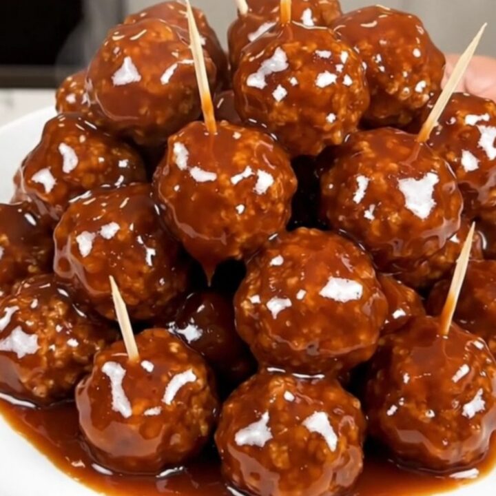 A close-up view of glazed beef meatballs in a slow cooker, glistening with a dark honey and barbecue sauce.