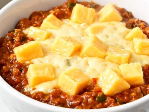 A top-down view of a slow cooker filled with a rich, melted chili cheese dip.
