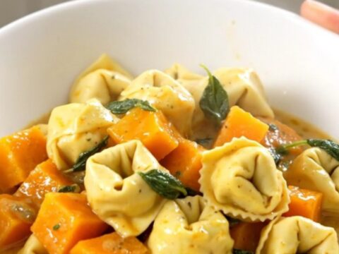 A close-up of a bowl filled with creamy cheese tortellini and tender butternut squash, garnished with fresh sage leaves.