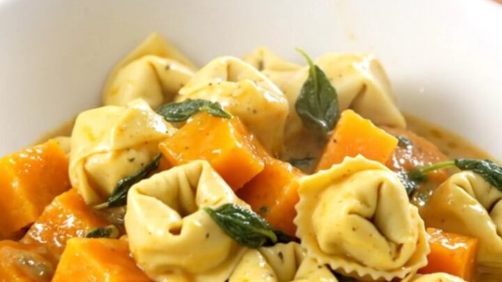 A close-up of a bowl filled with creamy cheese tortellini and tender butternut squash, garnished with fresh sage leaves.