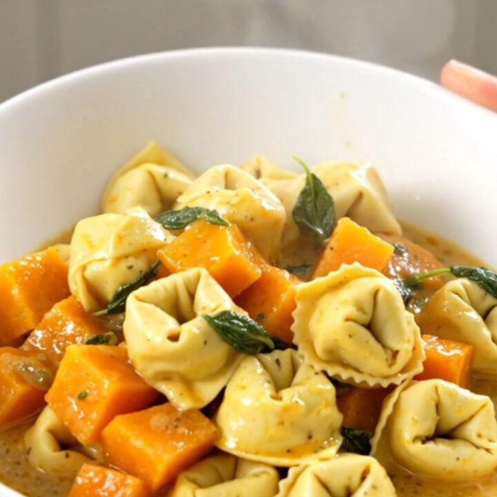 A close-up of a bowl filled with creamy cheese tortellini and tender butternut squash, garnished with fresh sage leaves.