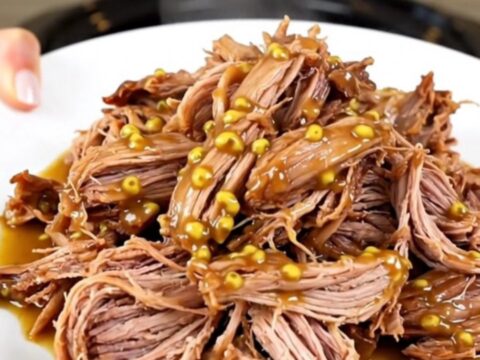 A plate of tender, glossy shredded mustard pulled pork with visible onion pieces.