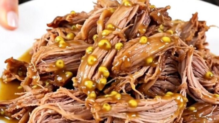 A plate of tender, glossy shredded mustard pulled pork with visible onion pieces.