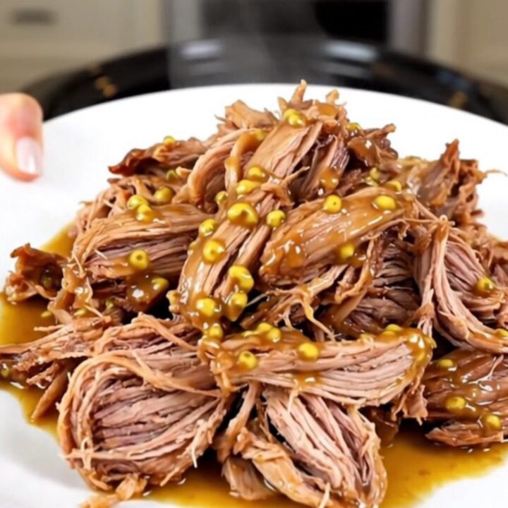 A plate of tender, glossy shredded mustard pulled pork with visible onion pieces.