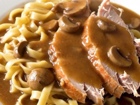 A slow cooker filled with raw turkey breast, sliced mushrooms, and creamy gravy base ready to cook.