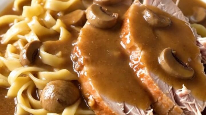 A slow cooker filled with raw turkey breast, sliced mushrooms, and creamy gravy base ready to cook.