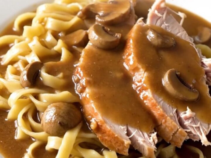 A slow cooker filled with raw turkey breast, sliced mushrooms, and creamy gravy base ready to cook.