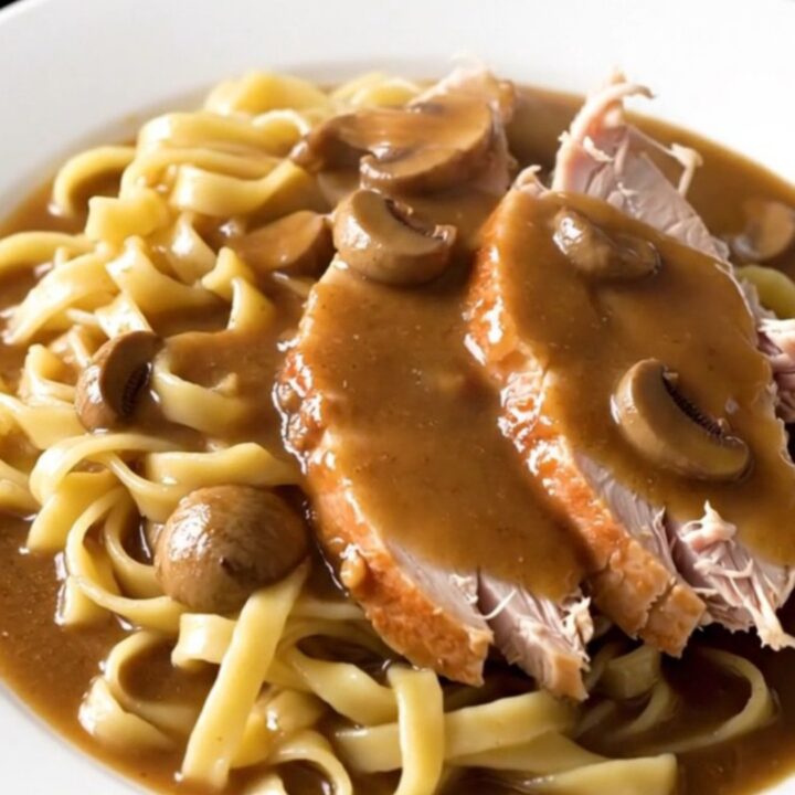A slow cooker filled with raw turkey breast, sliced mushrooms, and creamy gravy base ready to cook.