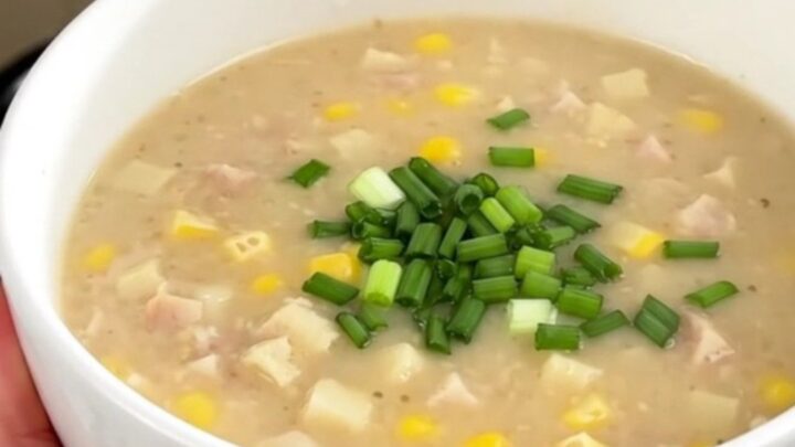 A bowl of creamy smoked sausage and corn chowder topped with fresh chives, against a blurred kitchen background.