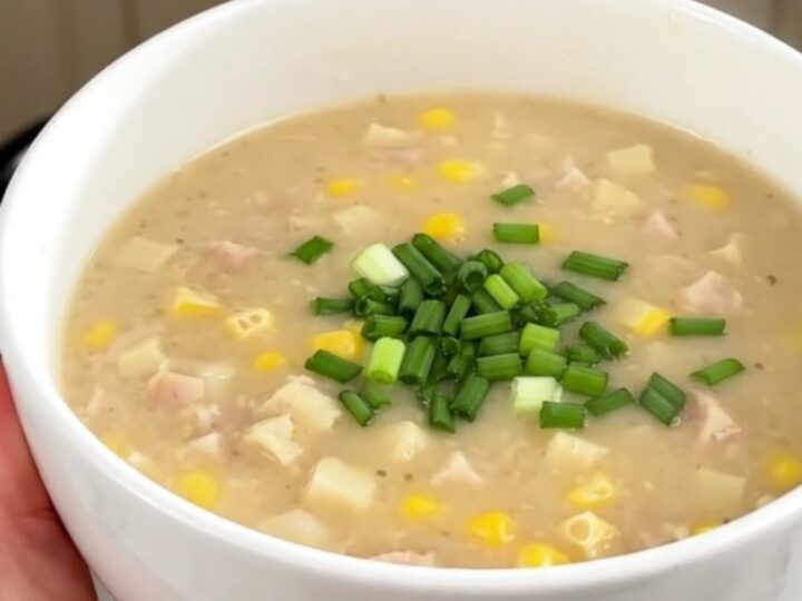 A bowl of creamy smoked sausage and corn chowder topped with fresh chives, against a blurred kitchen background.