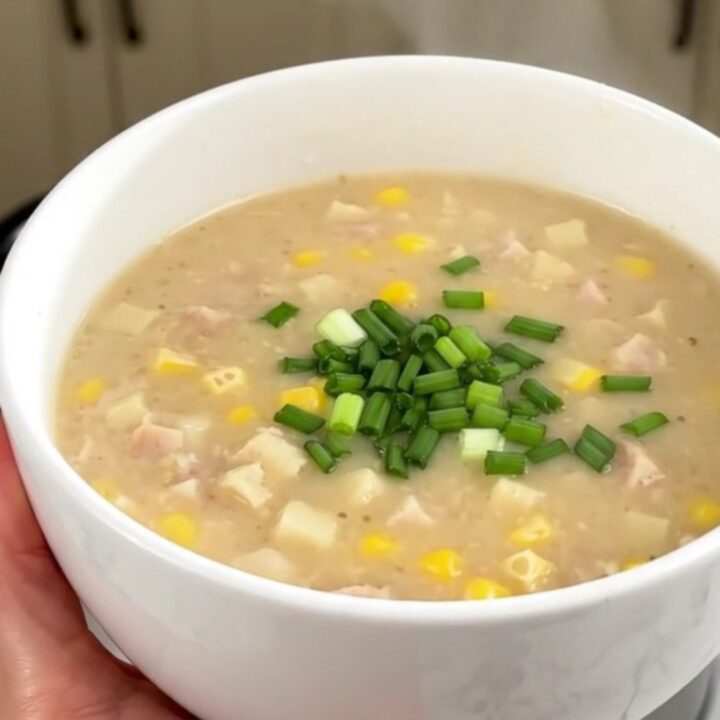 A bowl of creamy smoked sausage and corn chowder topped with fresh chives, against a blurred kitchen background.