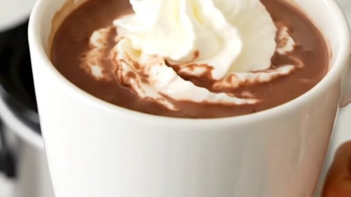A steaming mug of butterscotch hot chocolate topped with whipped cream on a wooden table.