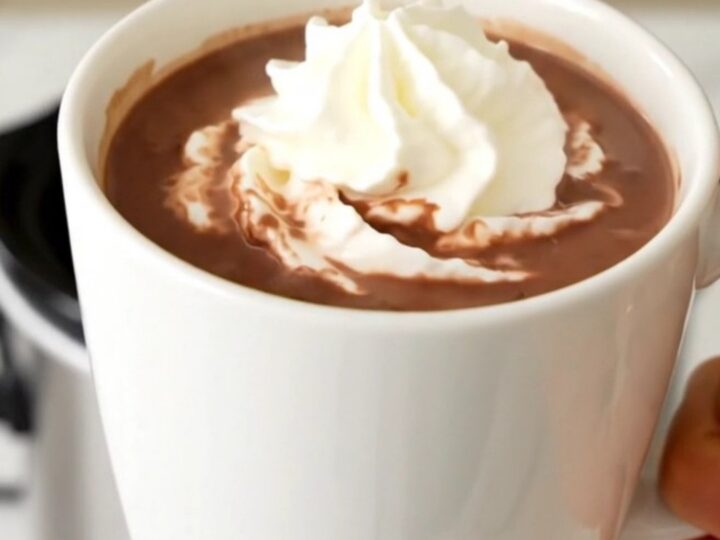 A steaming mug of butterscotch hot chocolate topped with whipped cream on a wooden table.