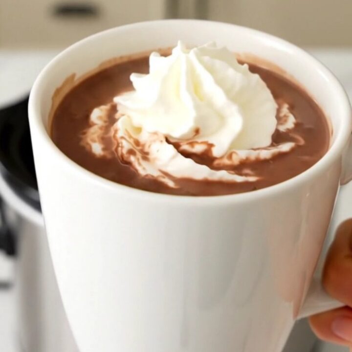 A steaming mug of butterscotch hot chocolate topped with whipped cream on a wooden table.