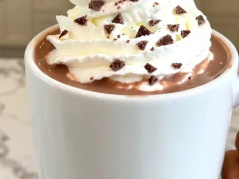 A steaming mug of peppermint hot chocolate topped with whipped cream on a table.
