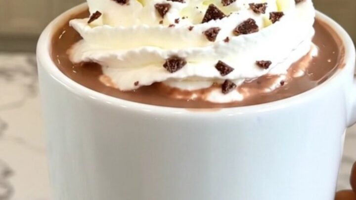 A steaming mug of peppermint hot chocolate topped with whipped cream on a table.