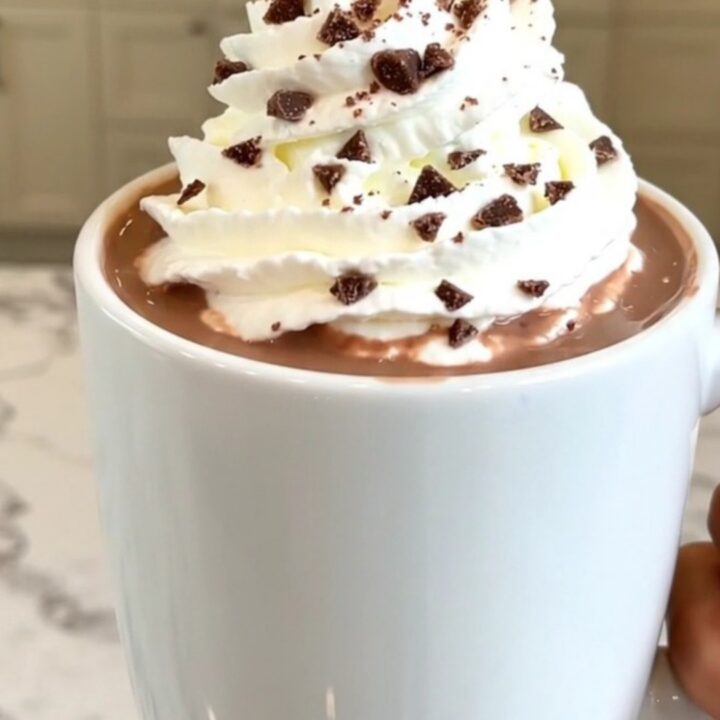 A steaming mug of peppermint hot chocolate topped with whipped cream on a table.