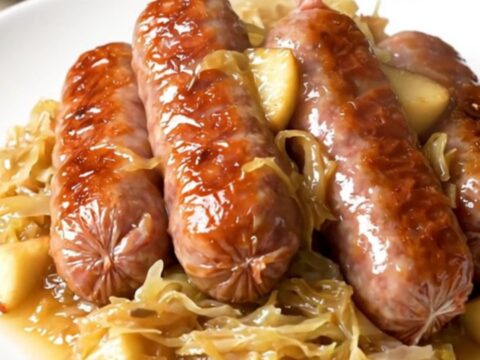 A top-down view of a slow cooker filled with bratwurst, sauerkraut, and shredded apples.